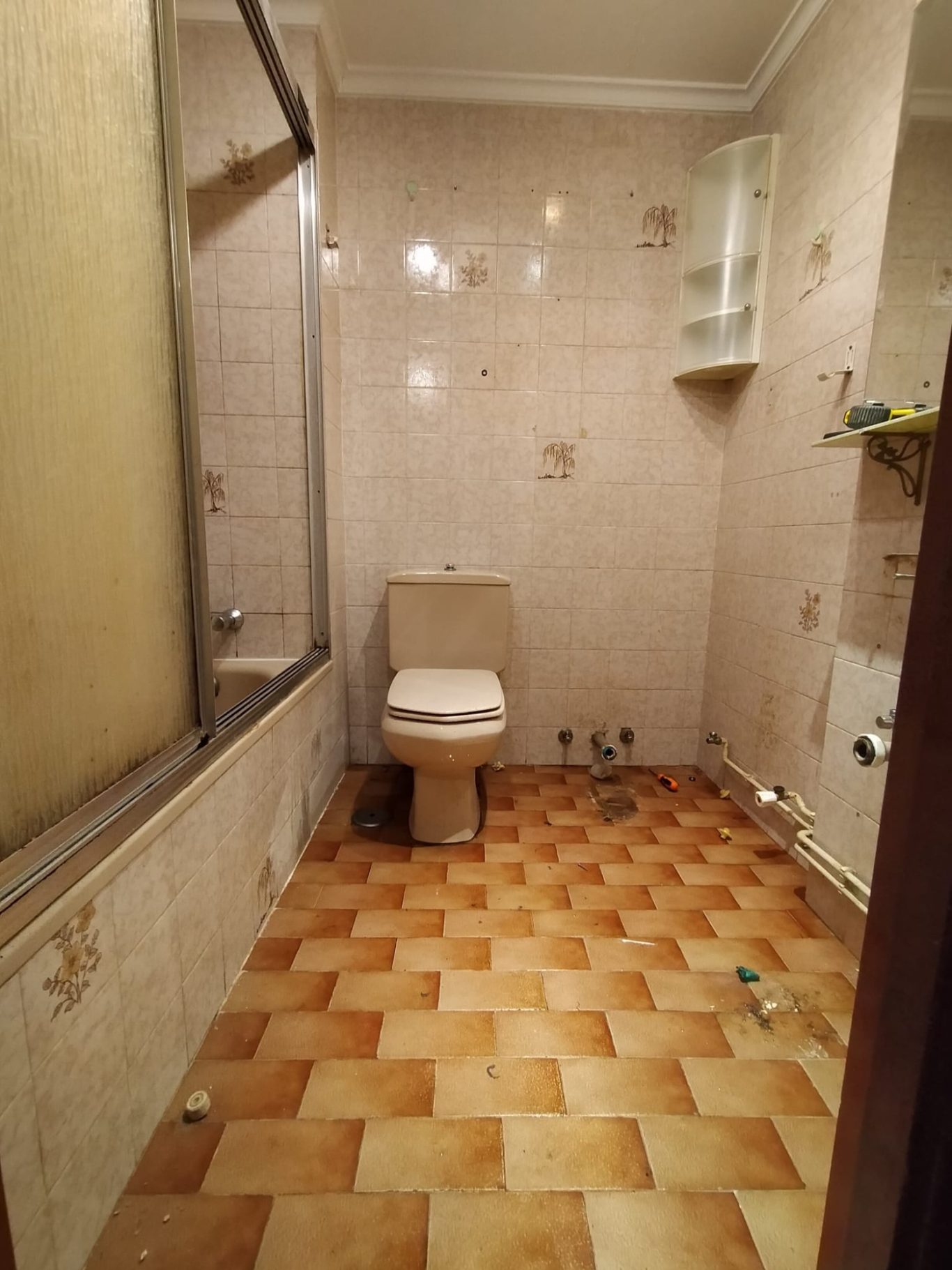 ANTES Baño con azulejos en el suelo, inodoro y ducha en una esquina. Paredes desgastadas.