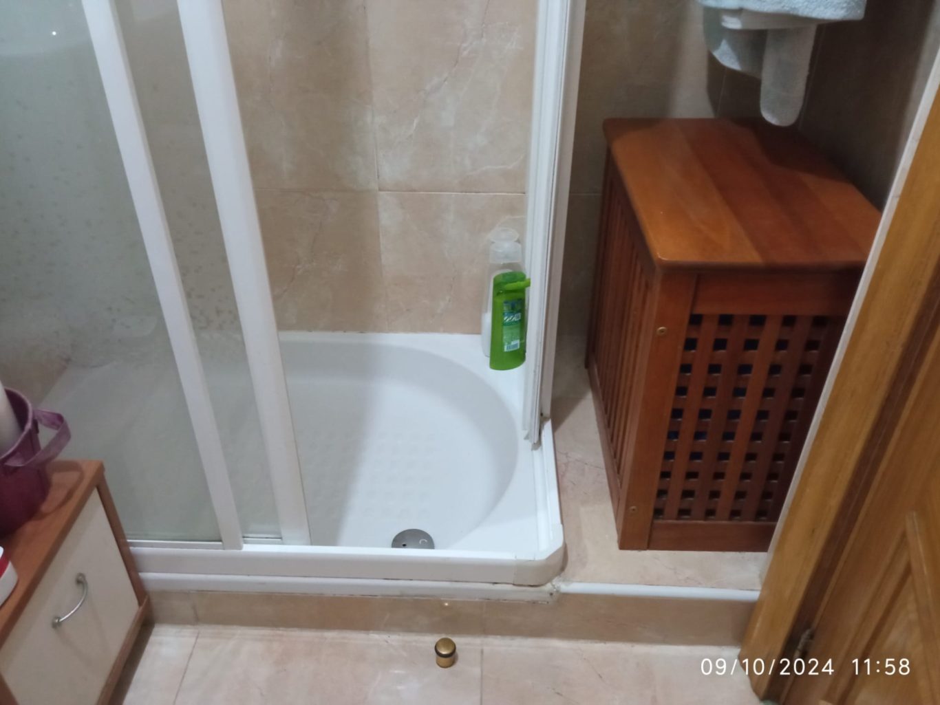 ANTES Duchas con mampara, caja de madera y productos de higiene en el suelo.