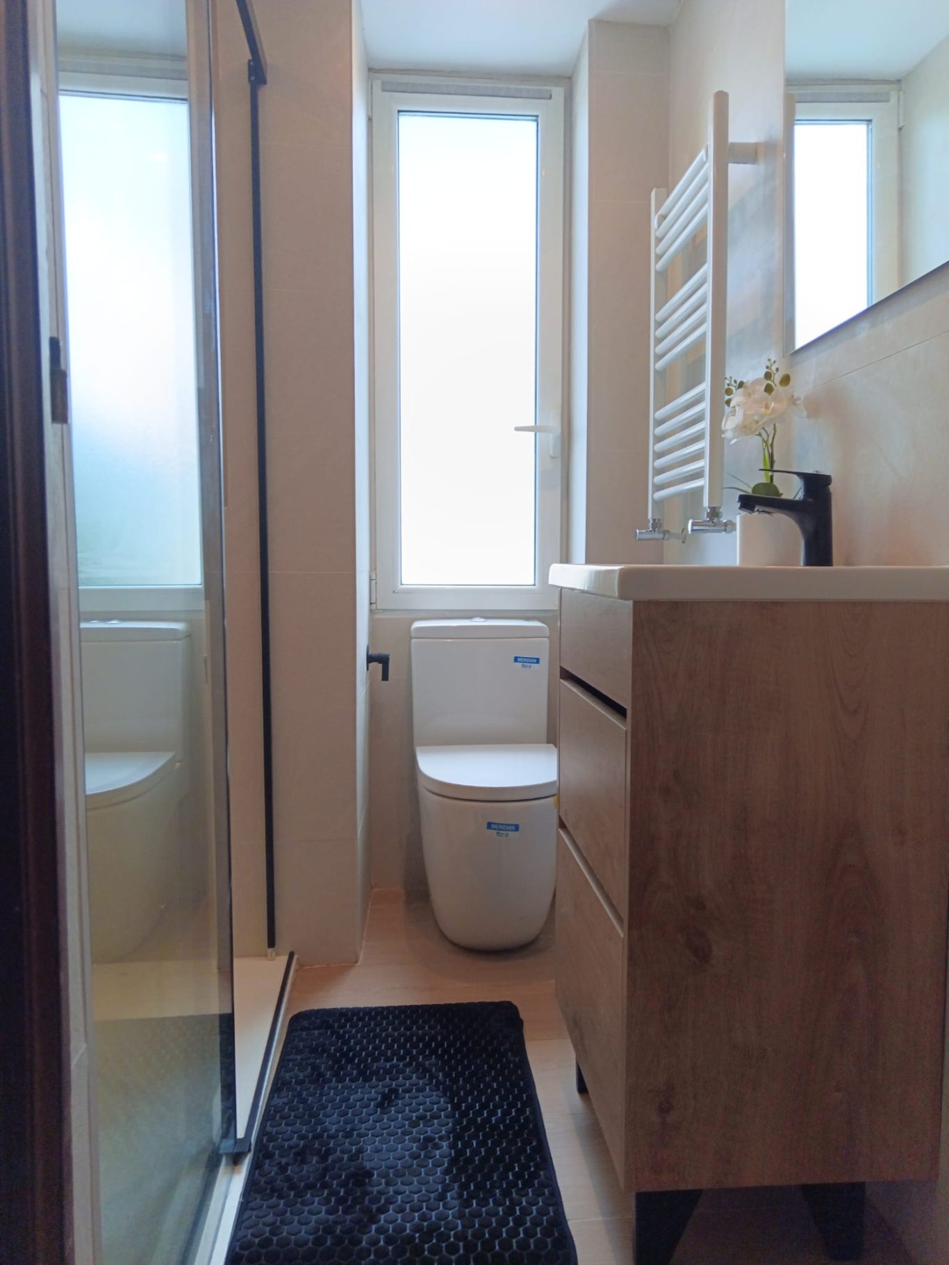 Baño moderno con ducha, inodoro y mueble de lavabo. Luz natural entra por las ventanas.