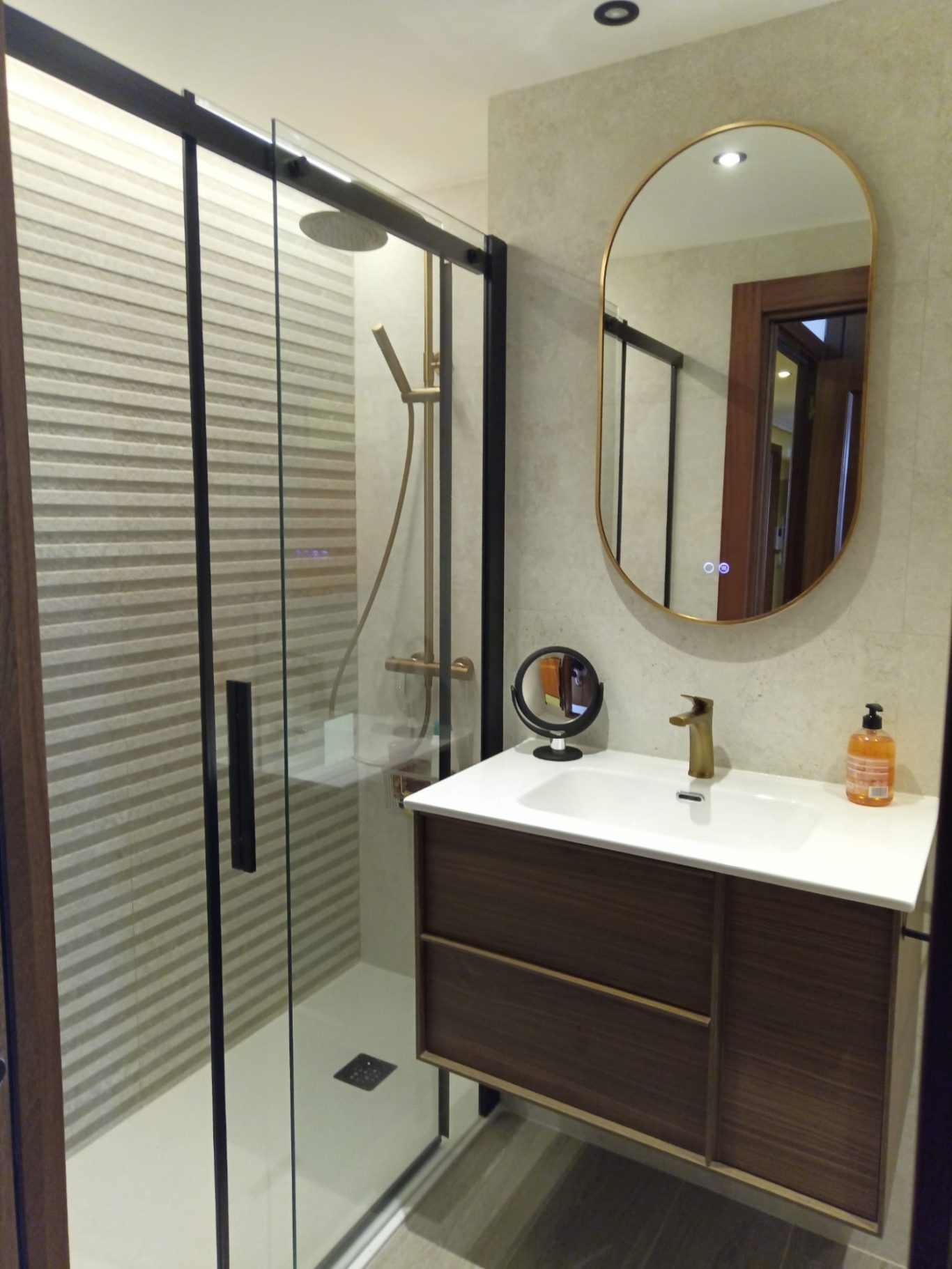 Baño moderno con ducha, lavabo de madera y espejo ovalado. Detalles en tonos neutros.